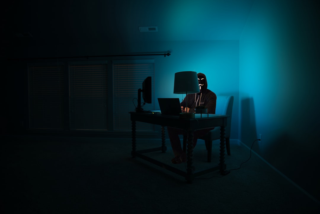 Anonymous hacker wearing a mask sitting in front of a laptop in the dark